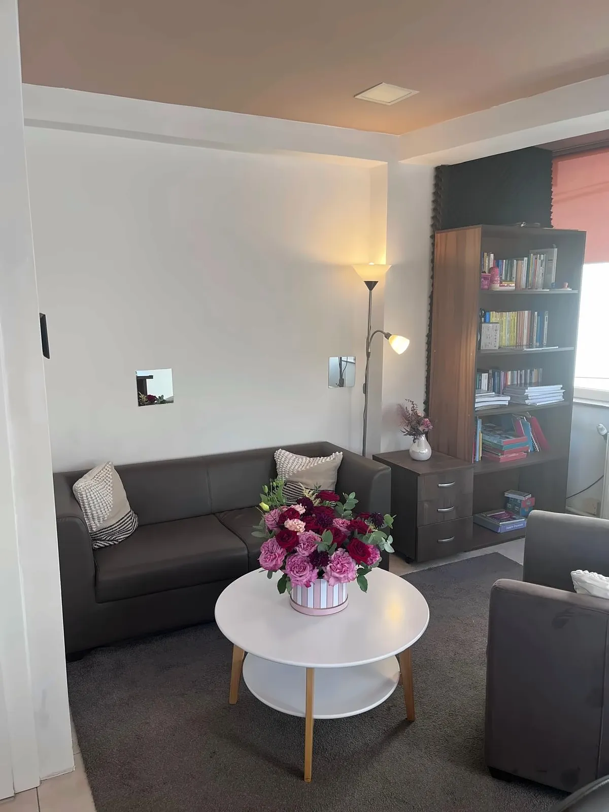 Camera de ședințe a cabinetului, cu canapea, fotolii, bibliotecă și un buchet de flori pe măsuță